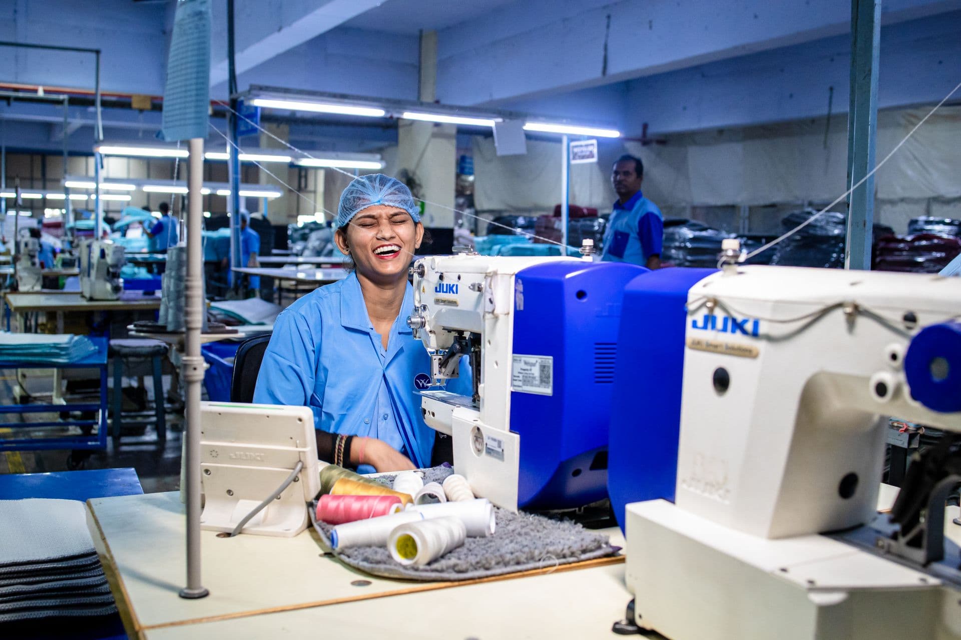 Garment worker at a sewing station beside coloured thread cones